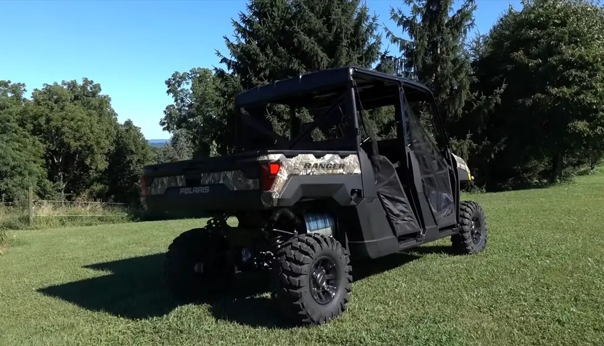 A Polaris Ranger Crew XP 1000 is parked in a green field. In the background there are trees and beautiful blue sky.