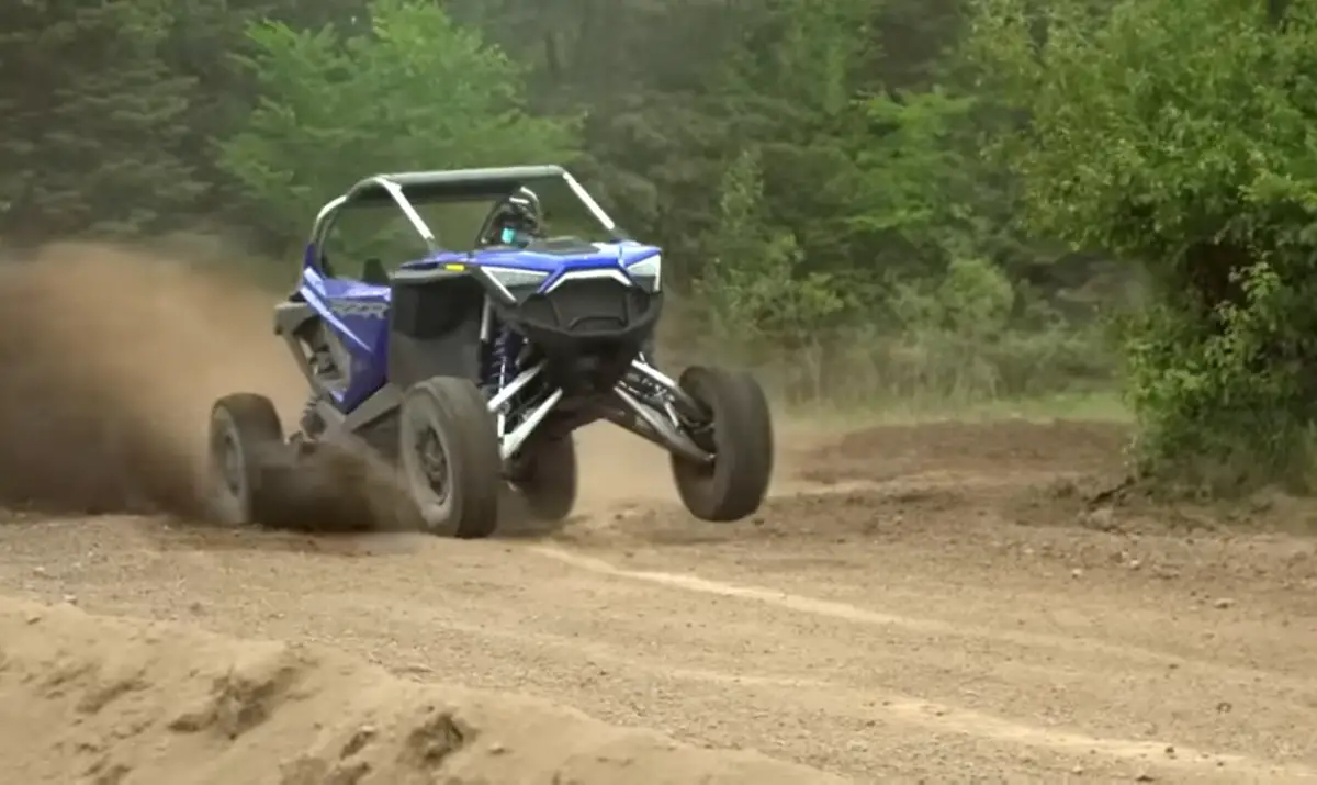 A Polaris RZR UTV is being driven through a dirt and dusty road.