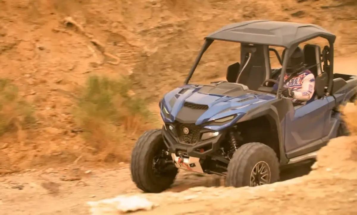 A Yamaha Wolverine RMAX2 1000 is being driven through a dirt road.