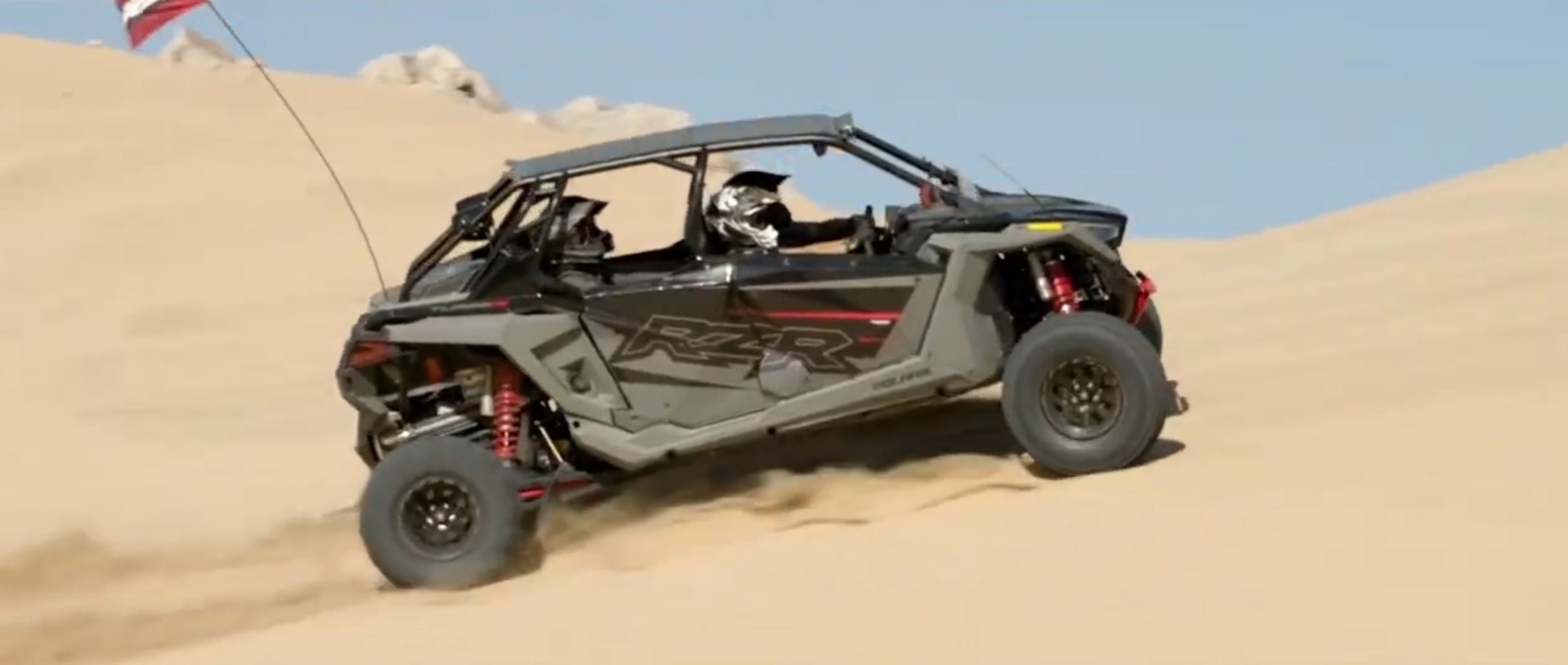 A Polaris RZR is being driven through a sandy desert road.