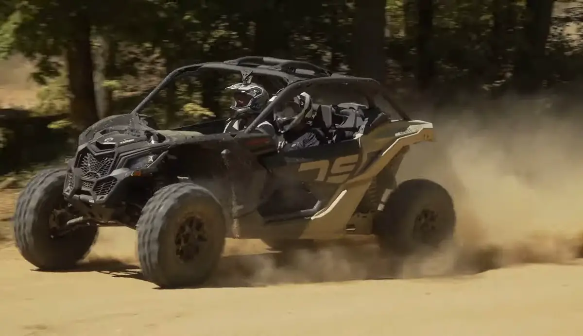 A Can-am Maverick X3 is being driven through a dirt and dusty road.