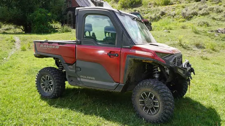 A red Polaris Ranger is parked on a grassy field for weight comparison.
