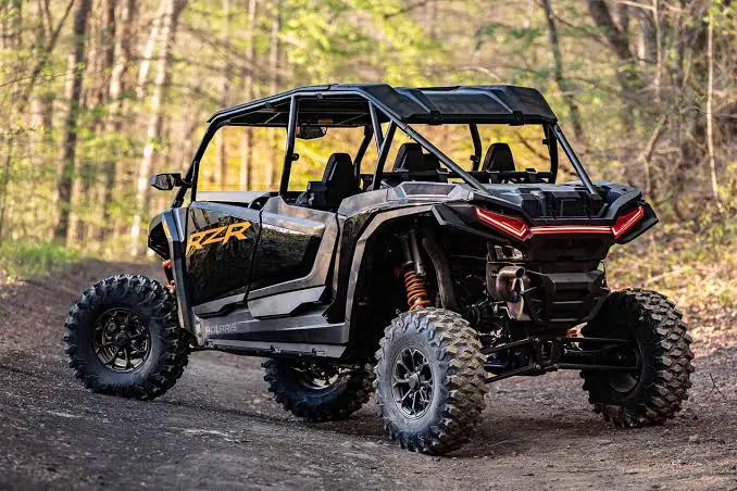 A Black Polaris RZR UTV is parked on a dirt road in a forest for weight comparison.