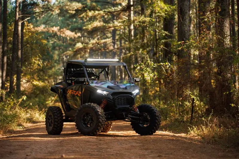 A Black Polaris RZR is parked on a dirt road in a forest for weight comparison.