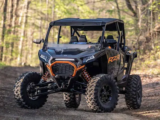 A Black Polaris UTV is parked on a dirt road for weight comparison in a forest. It's a sunny day and there are trees and bushes in the background.