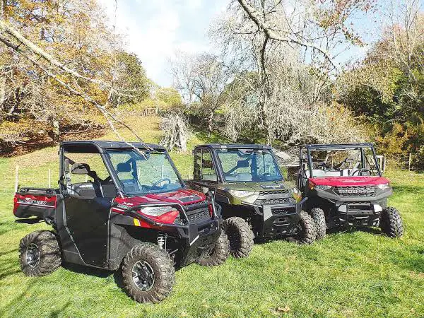 Three UTVs parked on a grassy field for weight comparison. Its a sunny day and there are trees and blue sky in the background.