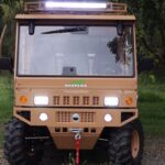 A Tuatara UTV with lights on is parked on a grassy field under a tree.