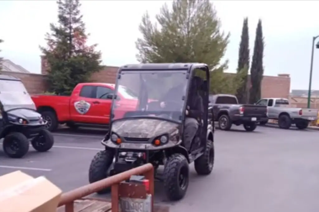 A tracker electric UTV is parked in a parking lot. In the background there are some other cars are parked.