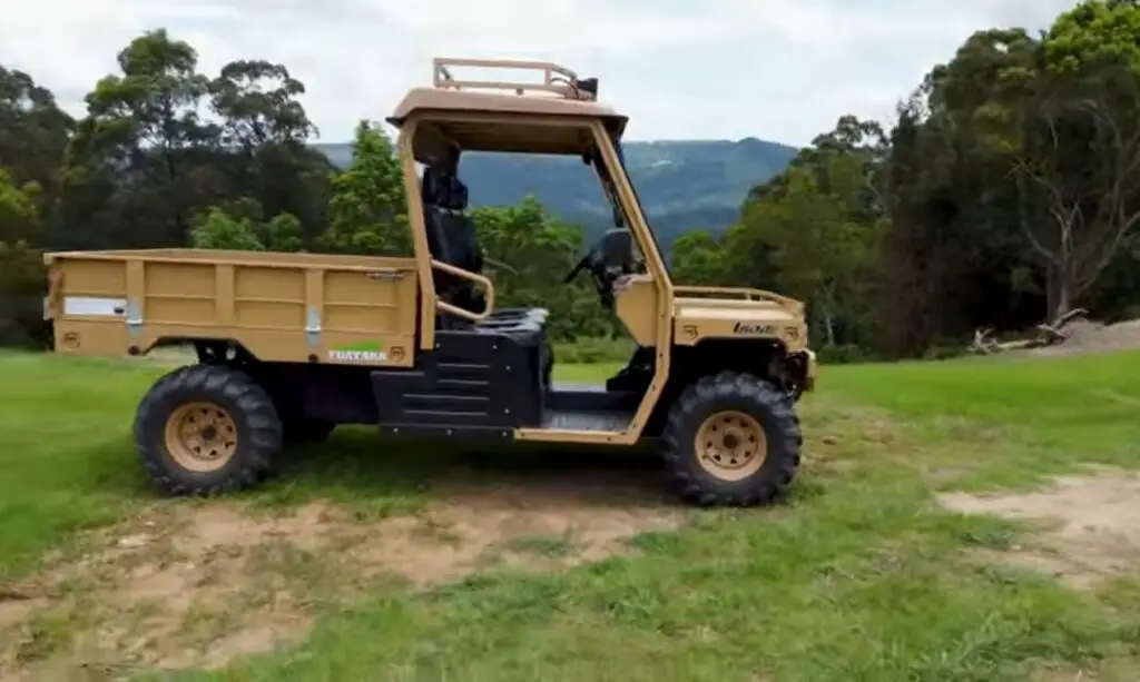 A Tuatara UTV is parked in a green field. In the background there are trees, mountains and beautiful blue sky.