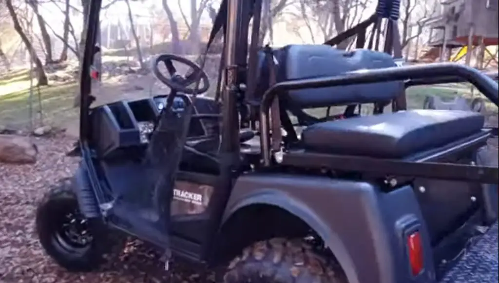 A Tracker electric UTV is parked under some trees. 
