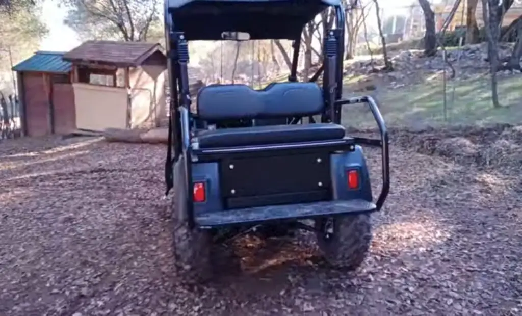 A tracker electric UTV is parked on a dirt surface under some trees.