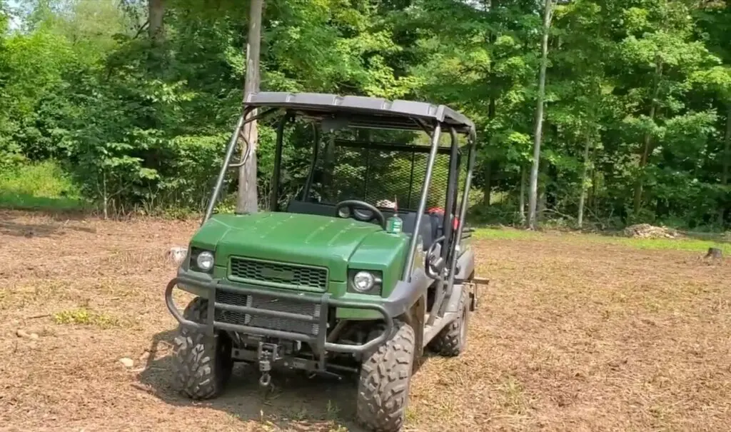 A Kawasaki UTV with food plot attachments is parked on a dirt field.