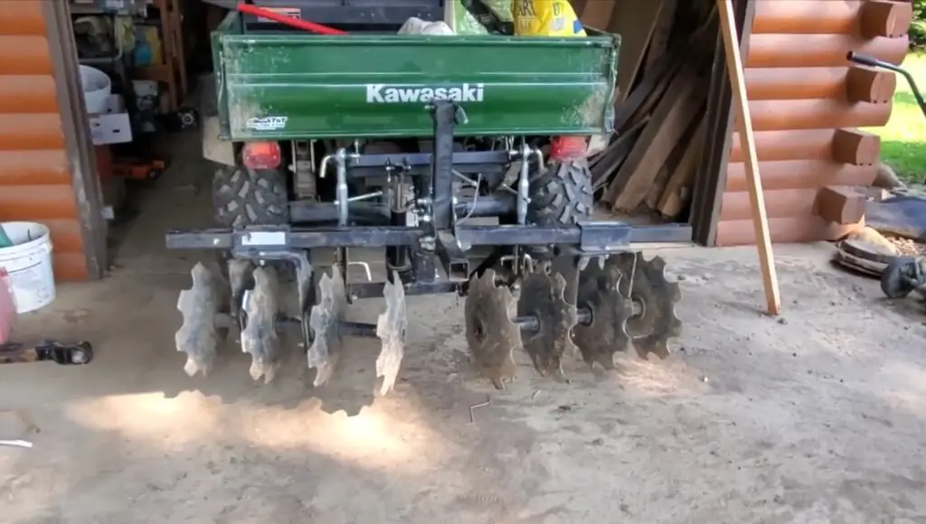 A Kawasaki side by side with food plot attachments is parked in a room.