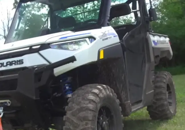 A Polaris UTV is parked on a grassy field close to a jungle 