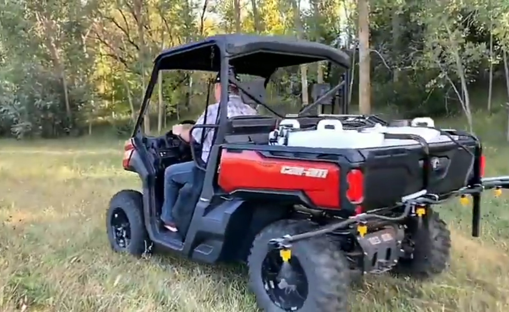 A can-am UTV with UTV sprayer is parked in a dry grass field.