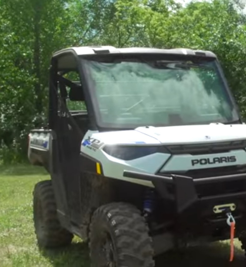 A Polaris Ranger XP Kinetic is parked on a grassy field. In the background there are trees and bushes.