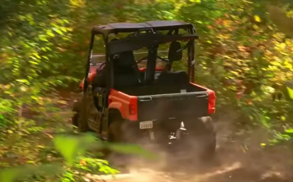 A Yamaha rhino 700 is being driven through a green forest 