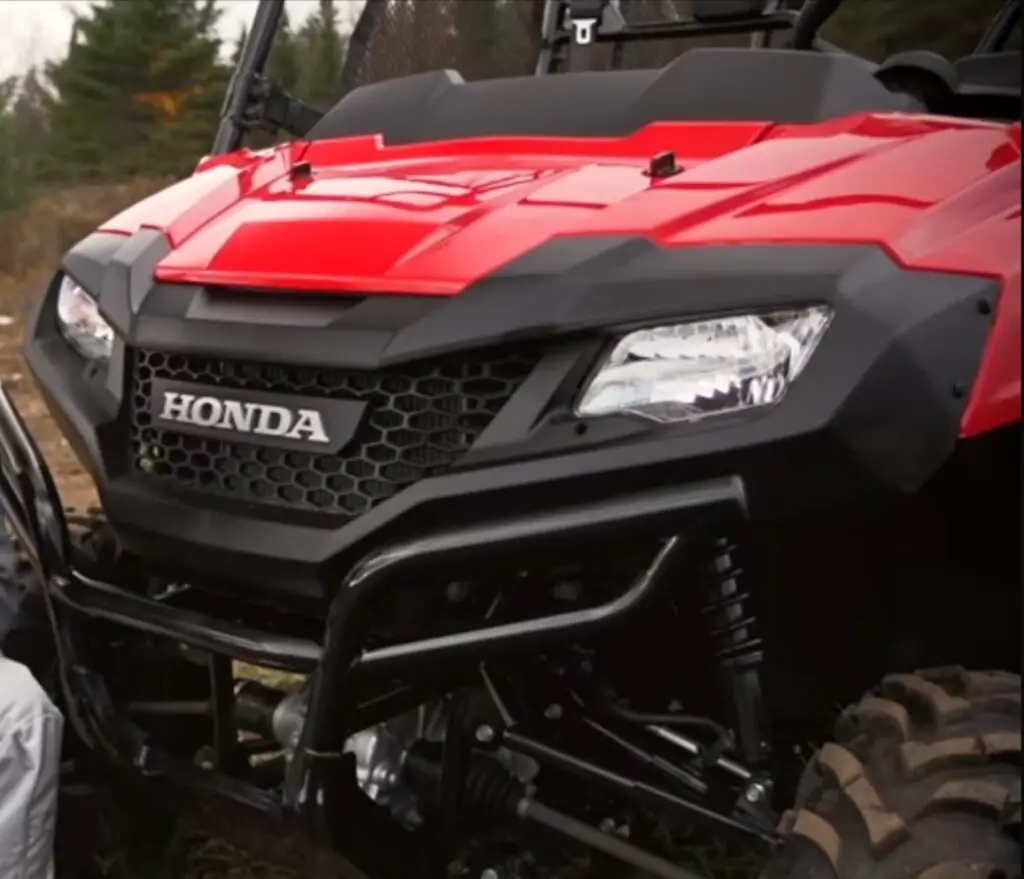 A Honda Pioneer 700 is parked on a dirt surface.