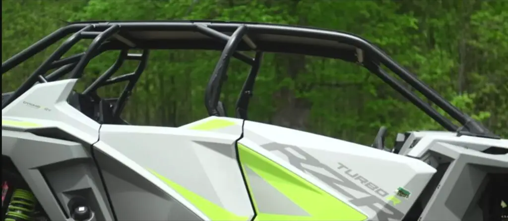 A Polaris RZR is parked on a dirt road close to a forest.