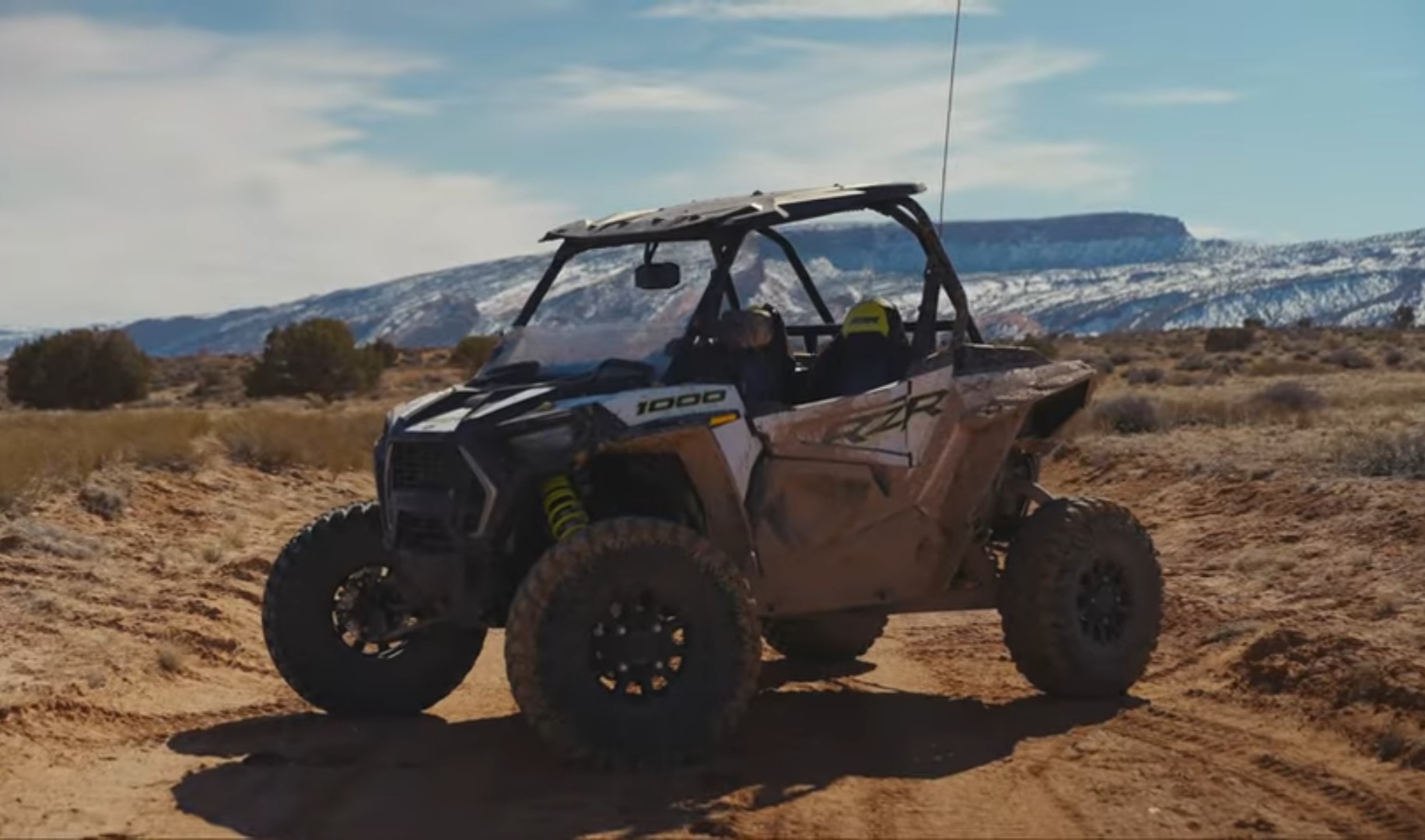 A Polaris RZR 1000 is parked on a dirt road. In the background there are mountains and beautiful blue sky.