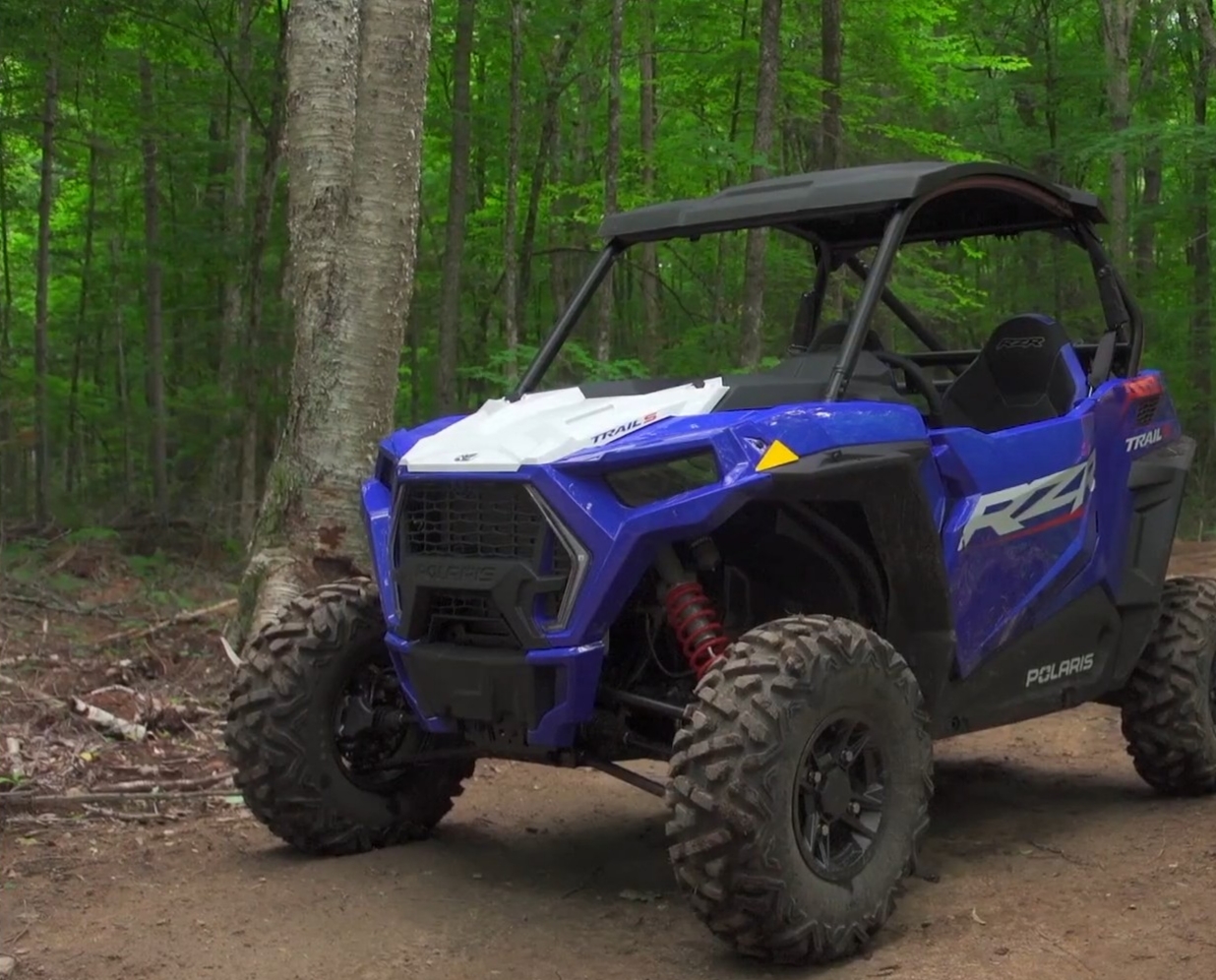 A Polaris RZR is parked on a dirt jungle road.