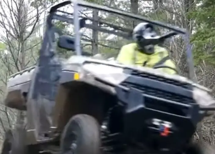 A Polaris Ranger UTV is being driven through a dirt road.