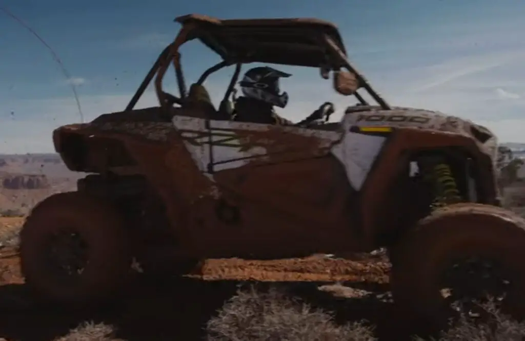 Polaris RZR 1000 is being driven through a dirt road.