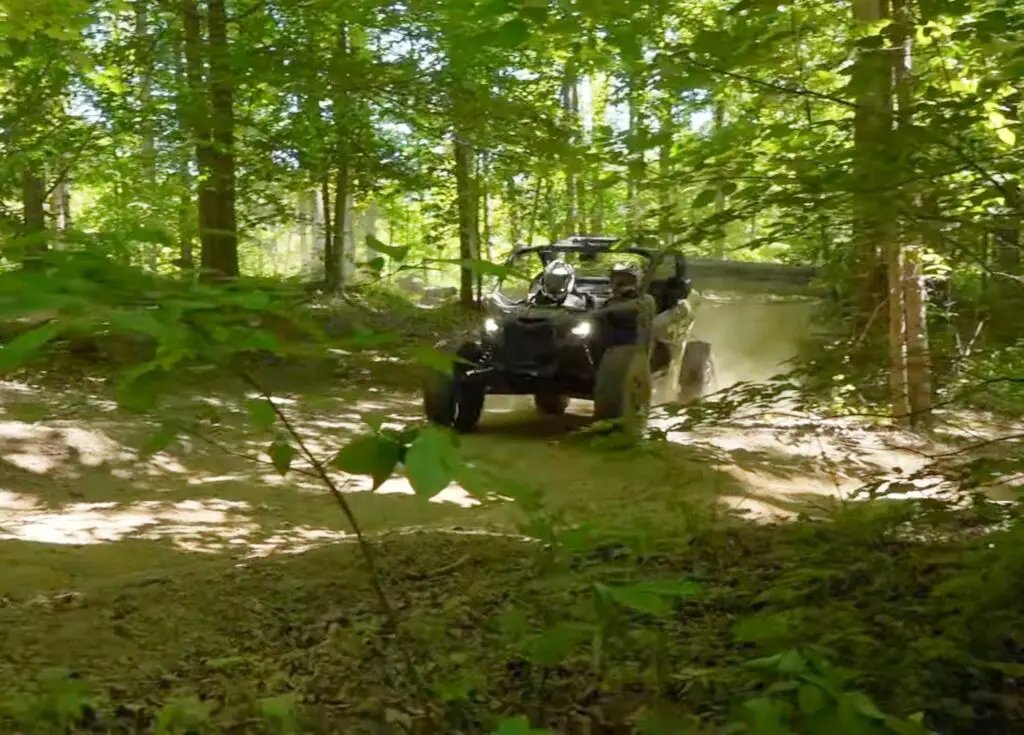 A Can-am Maverick X3 is being driven through a jungle terrain.