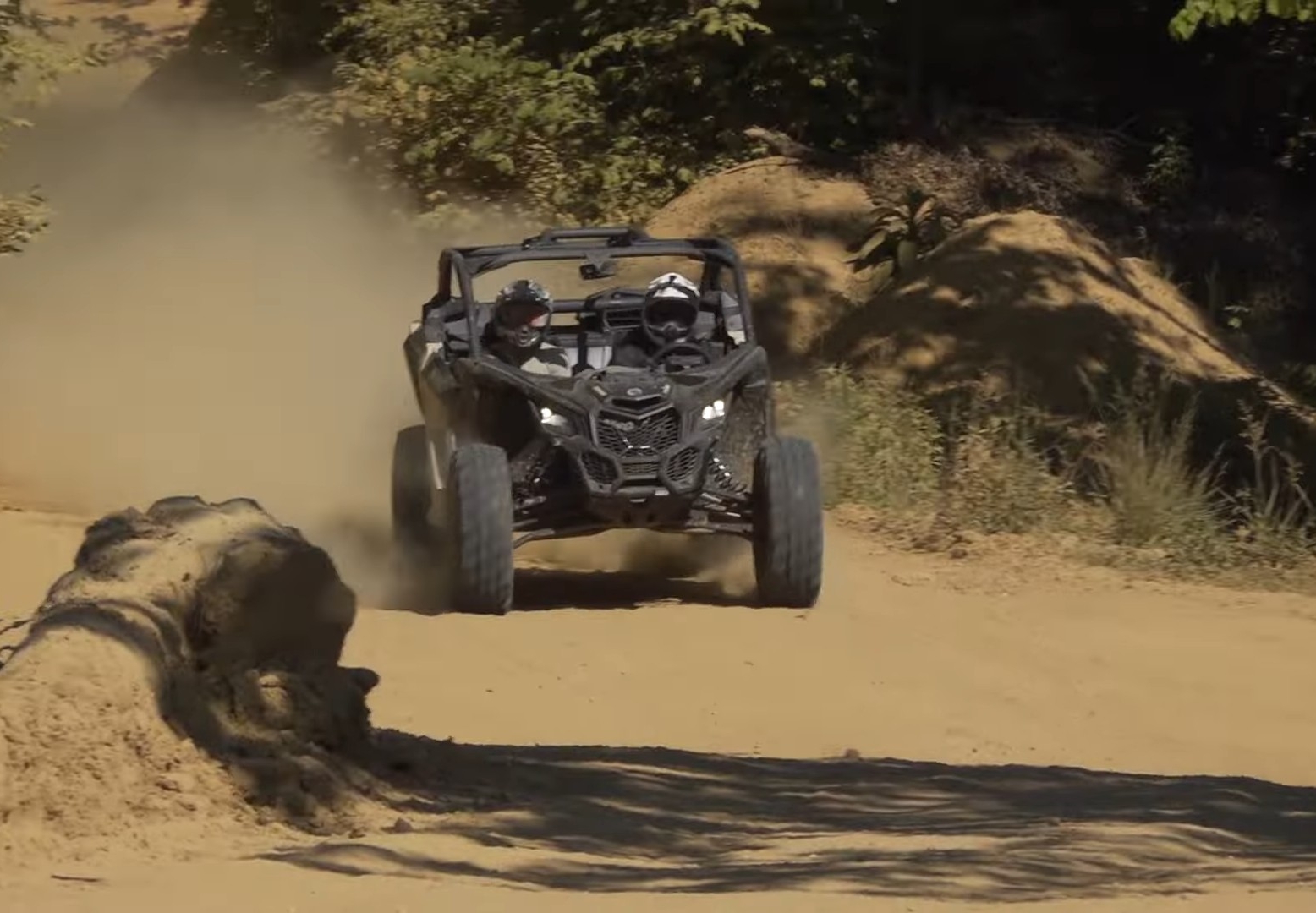 A Can-am Maverick X3 is being driven through a dirt and dusty road.