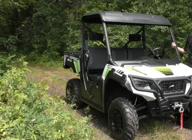 An Arctic cat Prowler pro is parked on a dirt road in front of a jungle.