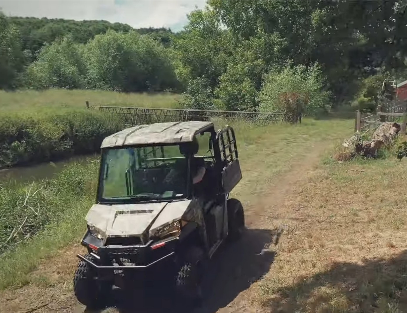 A Polaris Ranger EV is being driven through a dirt farm road.