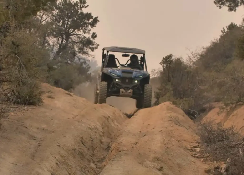 A Yamaha Wolverine RMAX2 is being driven through a desert dirt road.