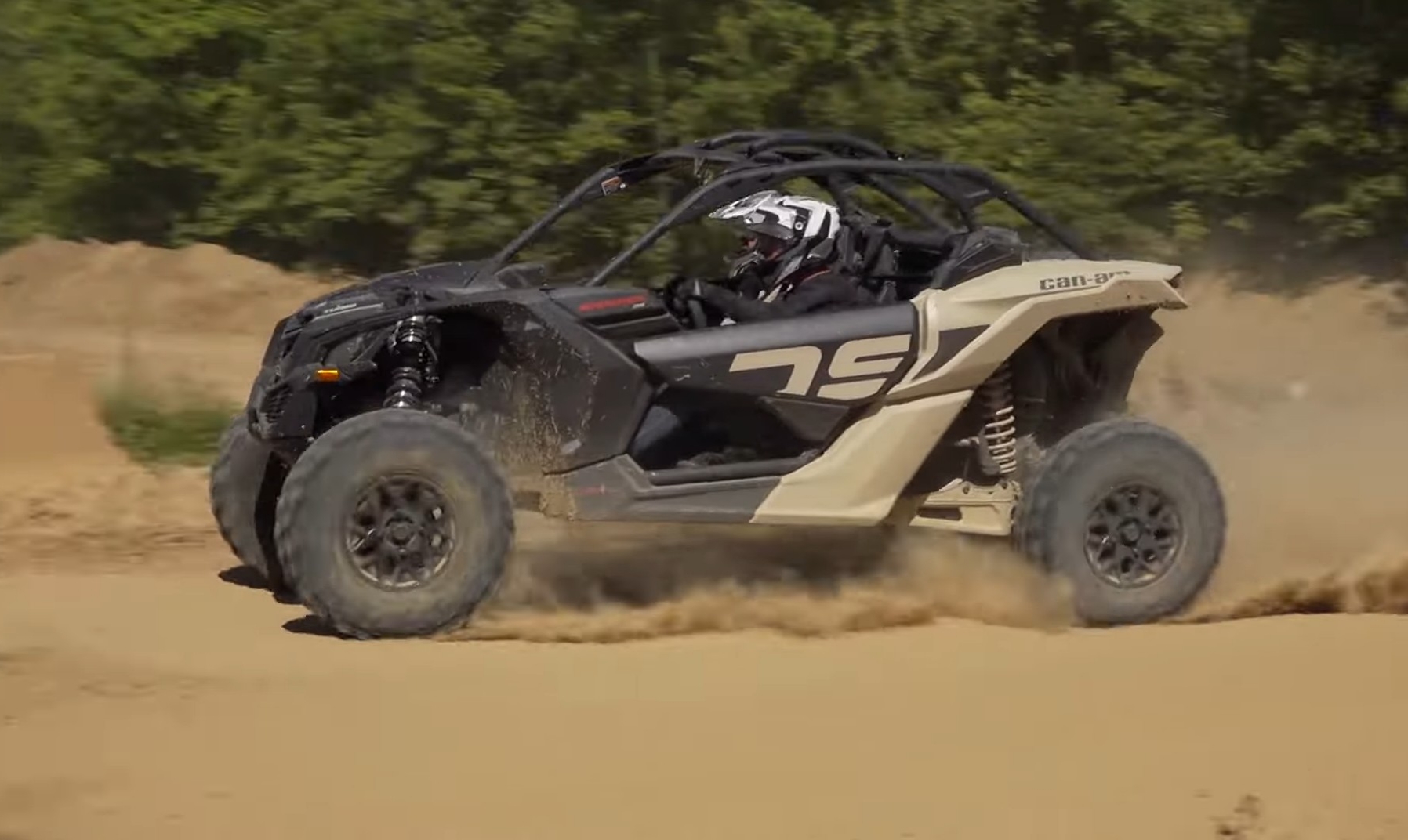 A Can-am Maverick X3 is being driven through a dirt road.