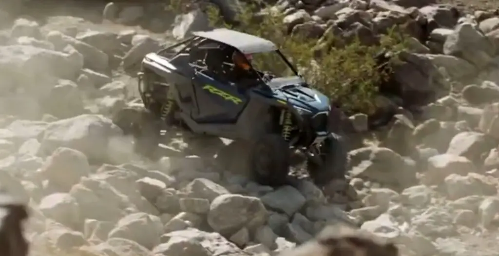 A Polaris RZR is being driven through a rocky mountain road.