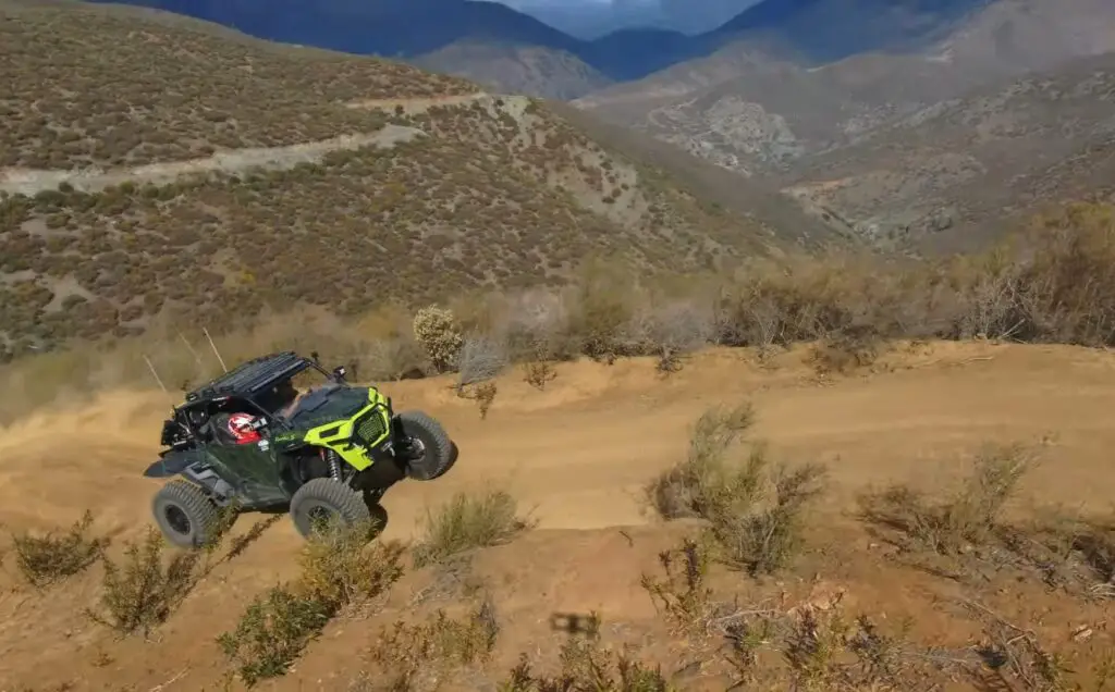 A Polaris Turbo is being driven through a California's dirt road. In the background there are mountains and beautiful blue sky.