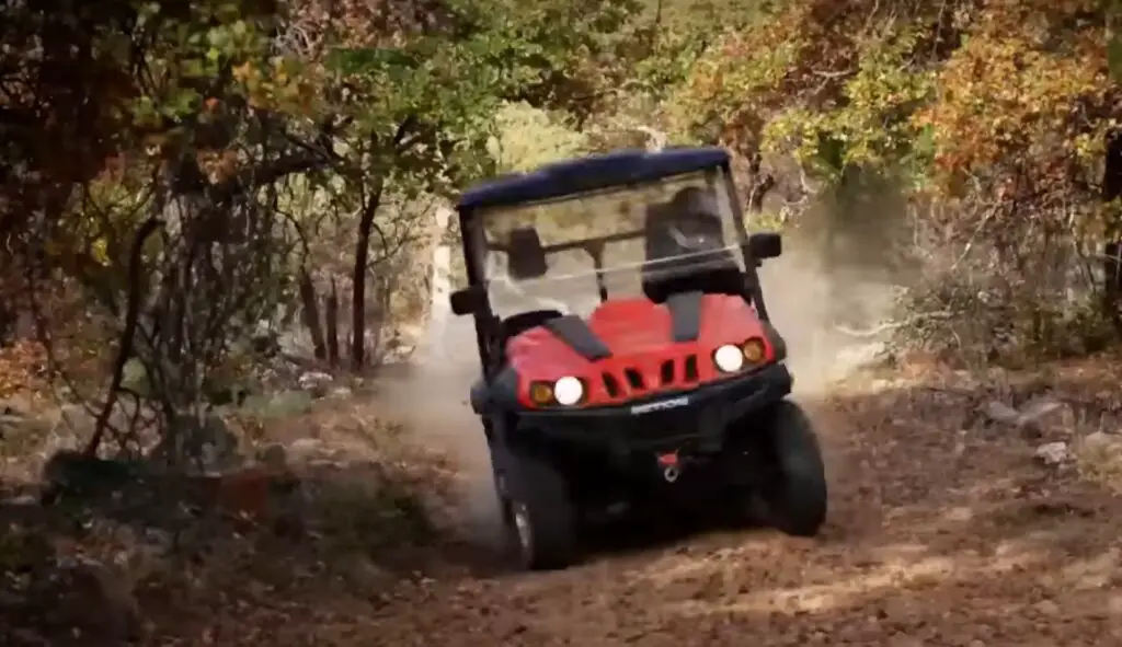 A red bennche UTV is being driven by a kid through a jungle terrain.