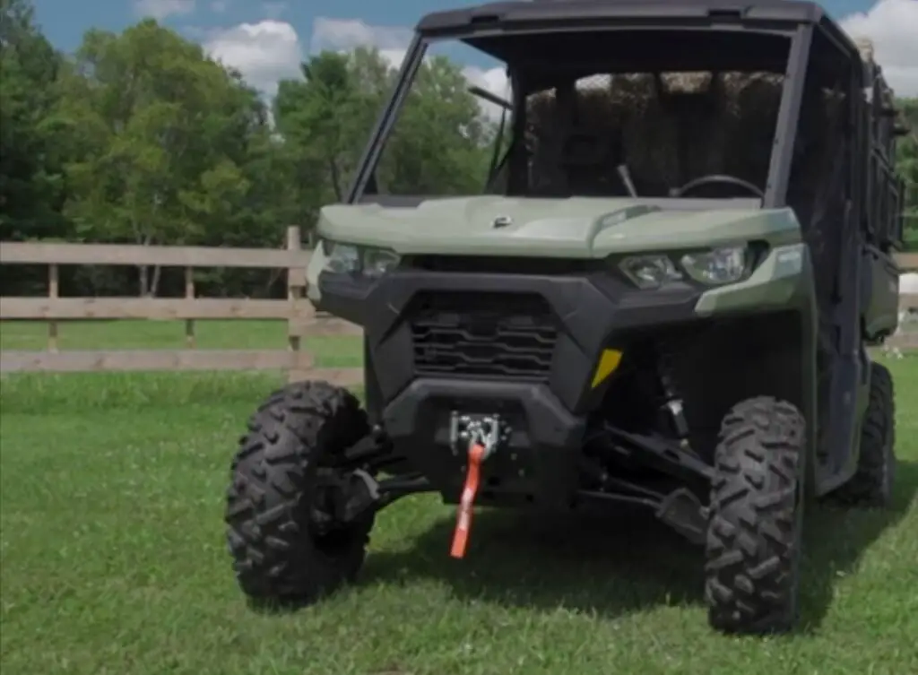 A Can-Am Defender HD10 is parked in a green field with fence.