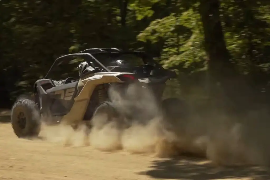 A Can-am Maverick X3 is being driven through a dusty jungle terrain.