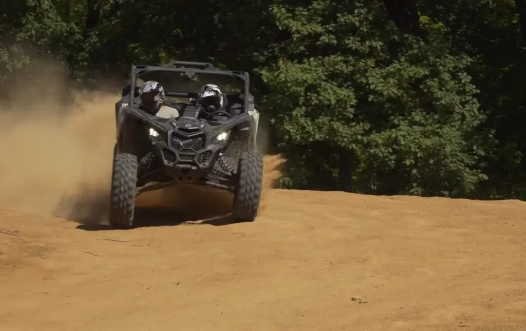 A Can-am Maverick X3 is being driven through a dusty trail.