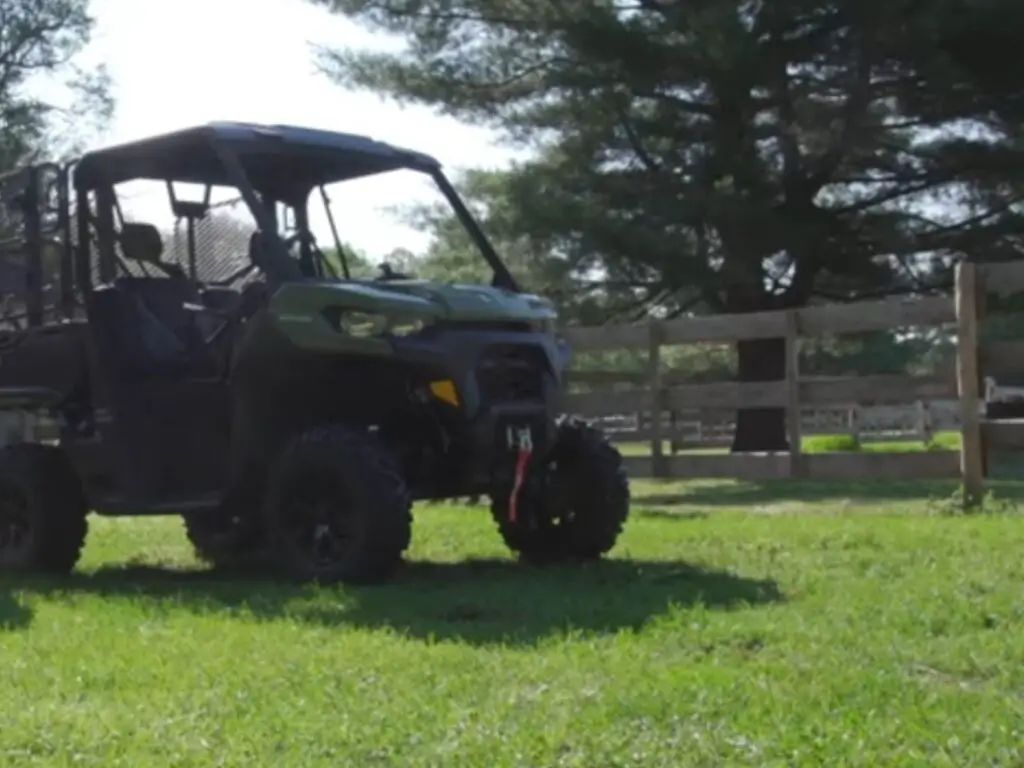 A Can-Am defender is parked in a green field with fence.