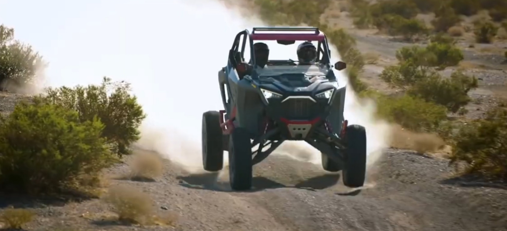 A Polaris UTV is being driven through a dirt and dusty road.