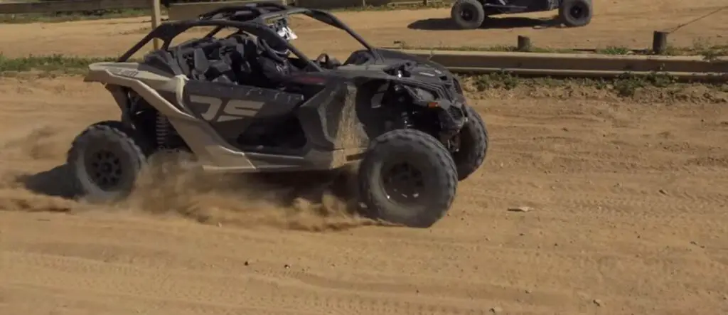 A Can-am Maverick X3 is being driven through a dusty road.