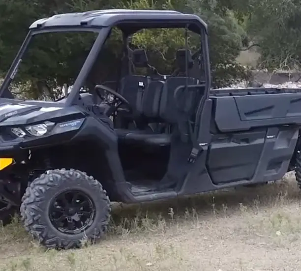 A Can-am defender pro XT is parked in front of some trees.