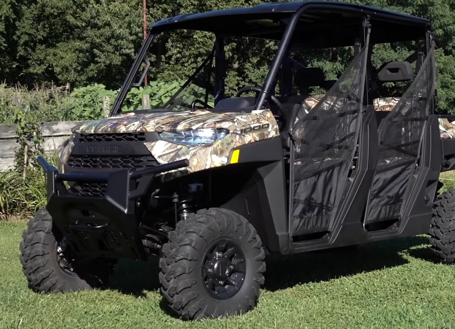 A Polaris Ranger Crew XP 1000 is parked on a grassy field. In the background there are trees and bushes.