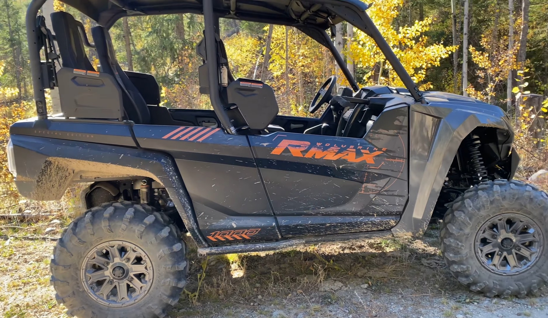 A Yamaha RMAX4 is parked on a dirt surface. In the background there are trees and bushes.