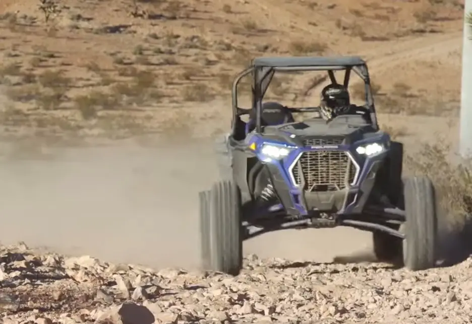 A Polaris RZR XP Turbo S is being driven through a dirt gravel road.