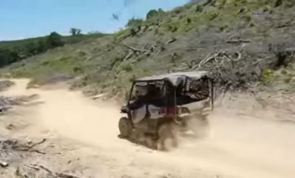 A Honda Pioneer 1000 is being driven through a dirt and dusty road.