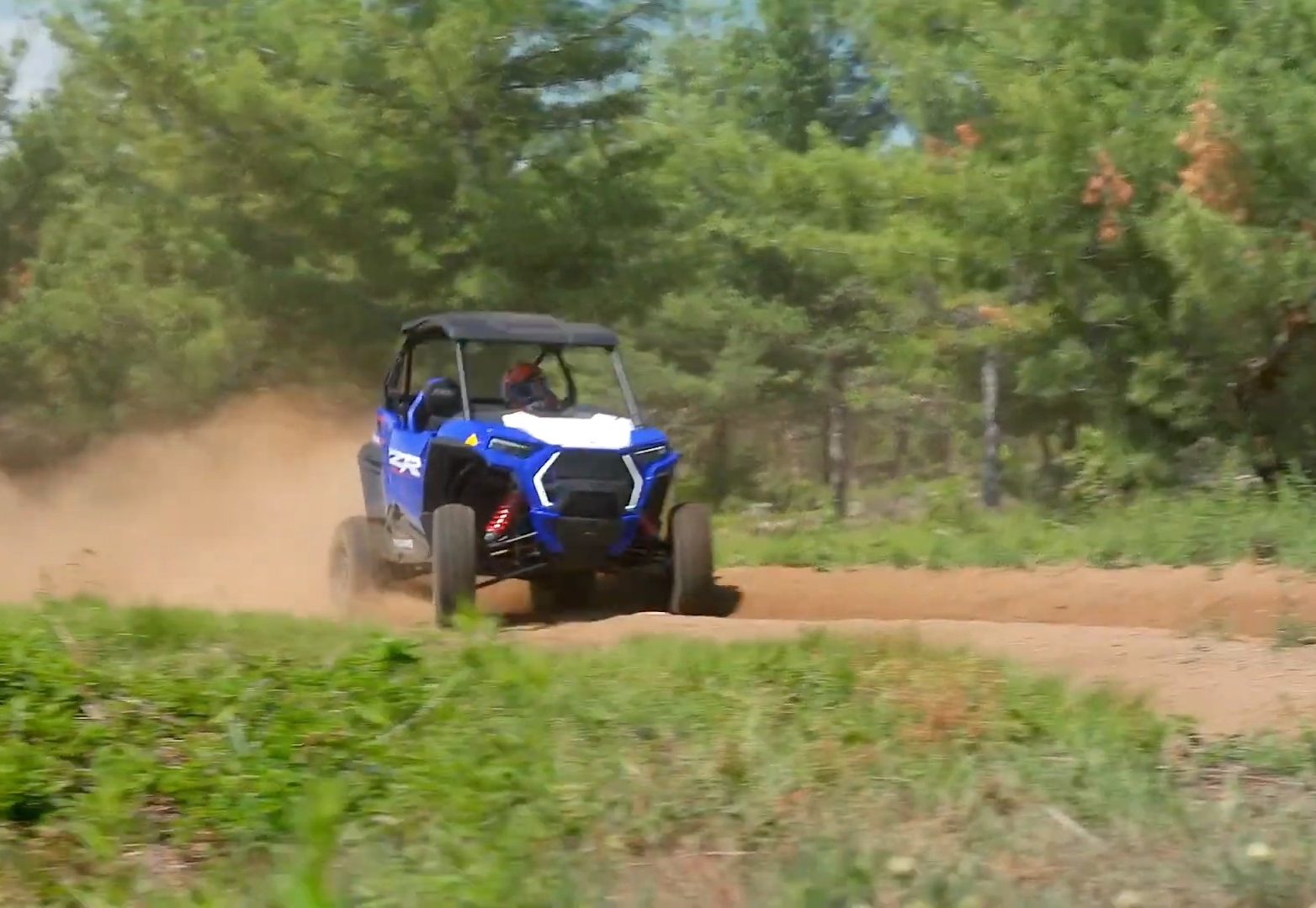 A Polaris RZR is being driven through a dirt and dusty trail.