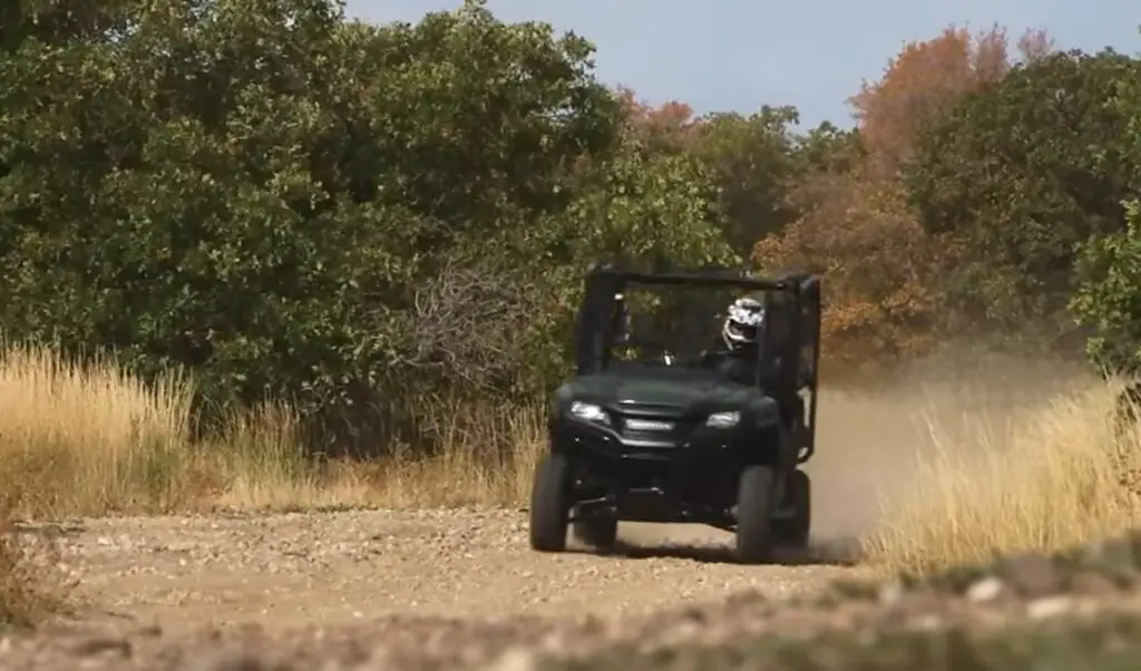 A Honda Pioneer 700 is being driven through a dirt and dusty road.