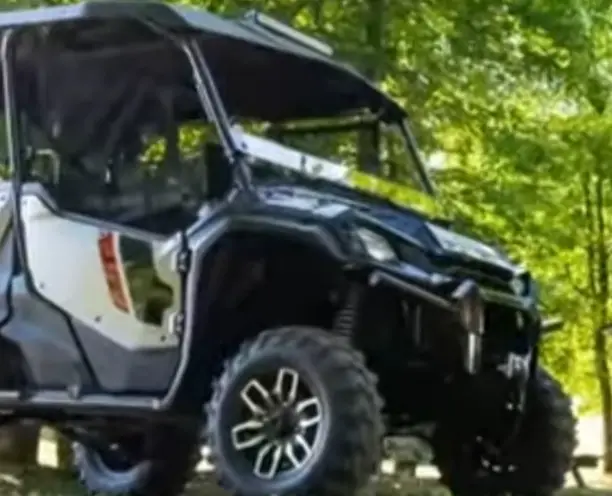 A Honda Pioneer 1000 is parked under some trees.